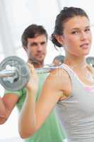 Fit young couple lifting barbells in gym