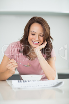 Woman with a bowl of cereals reading newspaper in kitchen