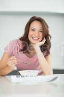 Smiling woman with bowl of cereals reading newspaper in kitchen