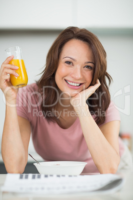 Woman with a bowl of cereals, orange juice and newspaper in kitc