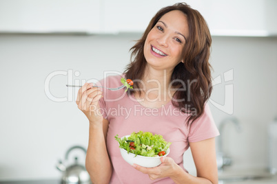 Portrait of smiling woman with a bowl of salad in kitchen