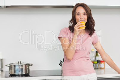 Smiling woman drinking orange juice in kitchen