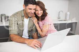 Happy couple using laptop in kitchen