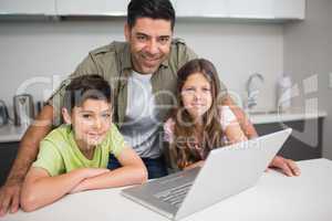 Smiling father with kids using laptop in kitchen