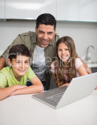 Smiling father with young kids using laptop in kitchen