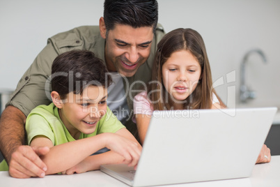 Father with young kids using laptop in kitchen