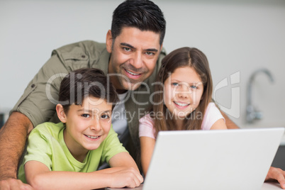 Smiling father with kids using laptop in kitchen