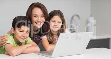 Smiling mother with kids using laptop in kitchen