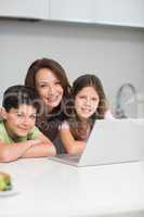 Smiling mother with kids using laptop in kitchen