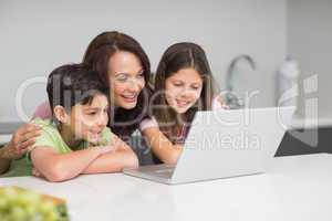 Smiling mother with kids using laptop in kitchen