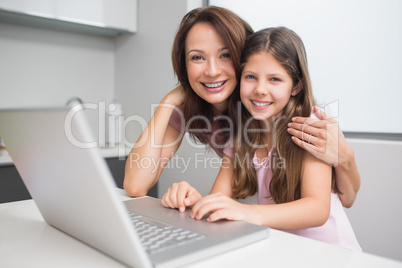 Smiling mother with daughter using laptop in kitchen