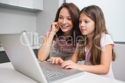 Smiling mother with daughter using laptop in kitchen