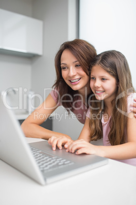 Smiling mother with daughter using laptop in kitchen