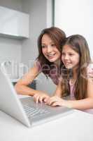 Smiling mother with daughter using laptop in kitchen