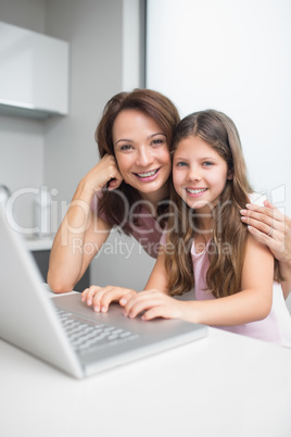 Smiling mother with daughter using laptop in kitchen