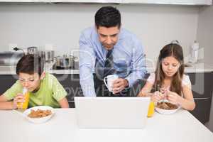Father using laptop and kids having breakfast in kitchen