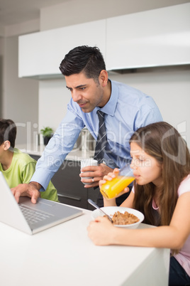 Father using laptop and kids having breakfast in kitchen