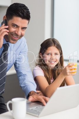 Smiling father with daughter using laptop in kitchen