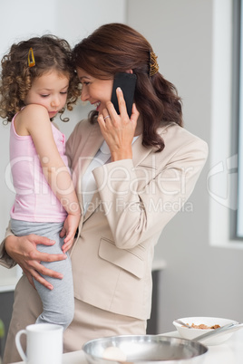 Well dressed mother carrying daughter while on call in kitchen