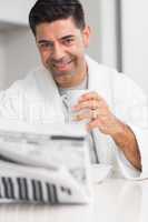 Smiling man with coffee cup reading newspaper in kitchen