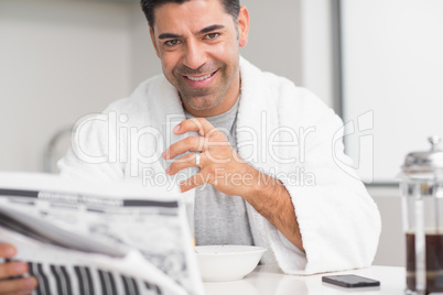 Smiling casual man with coffee cup reading newspaper in kitchen