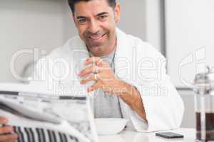 Smiling casual man with coffee cup reading newspaper in kitchen