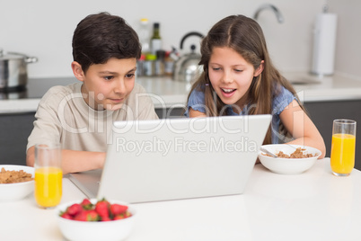 Smiling siblings enjoying breakfast while laptop in kitchen