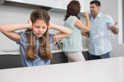 Sad girl covering ears while parents quarreling in kitchen