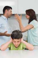 Boy covering ears while parents quarreling in kitchen
