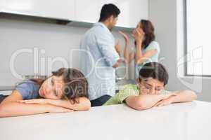 Sad young kids while parents quarreling in kitchen