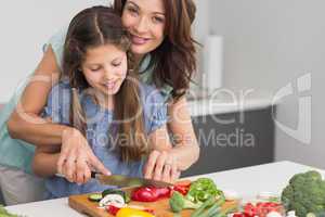 Smiling woman with daughter chopping vegetables in kitchen