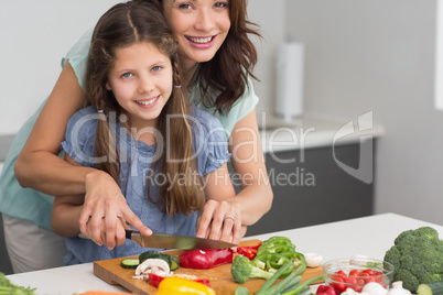 Smiling woman with daughter chopping vegetables in kitchen