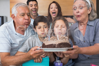 Extended family blowing candles on cake in living room