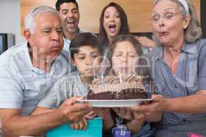 Extended family blowing candles on cake in living room