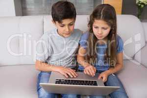 Young siblings using laptop in the living room