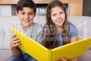 Portrait of smiling siblings with photo album in living room