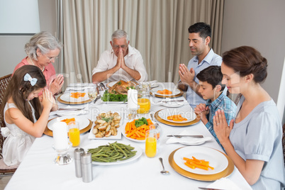 Family of six saying grace before meal at dining table