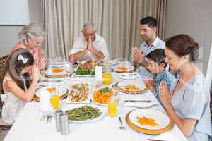 Family of six saying grace before meal at dining table