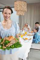 Woman holding chicken roast with family at dining table