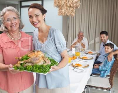 Woman and grandmother holding chicken roast with family at dinin