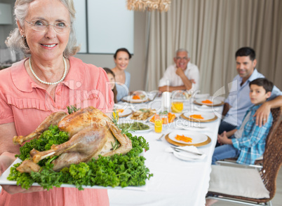 Grandmother holding chicken roast with family at dining table