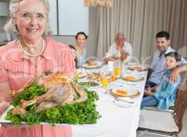 Grandmother holding chicken roast with family at dining table