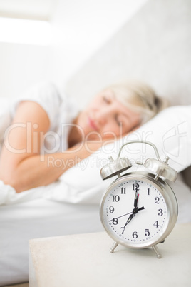 Woman sleeping in bed with alarm clock in foreground at bedroom