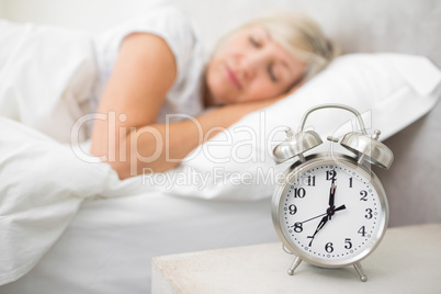 Woman sleeping in bed with alarm clock in foreground at bedroom