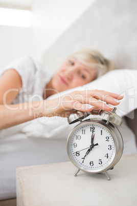 Woman extending hand to alarm clock in bed