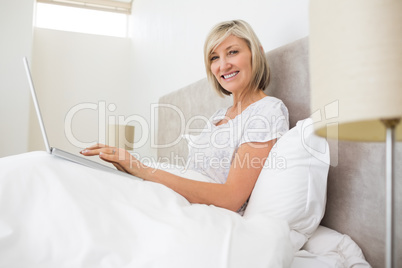 Portrait of a smiling woman using laptop in bed