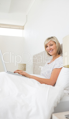 Smiling mature woman using laptop in bed