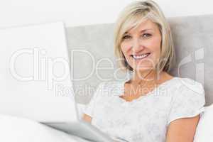 Smiling mature woman using laptop in bed