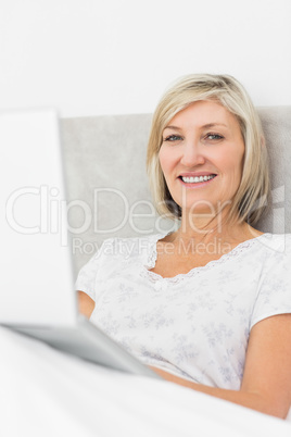 Smiling mature woman using laptop in bed