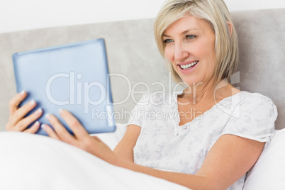 Smiling woman using digital tablet in bed